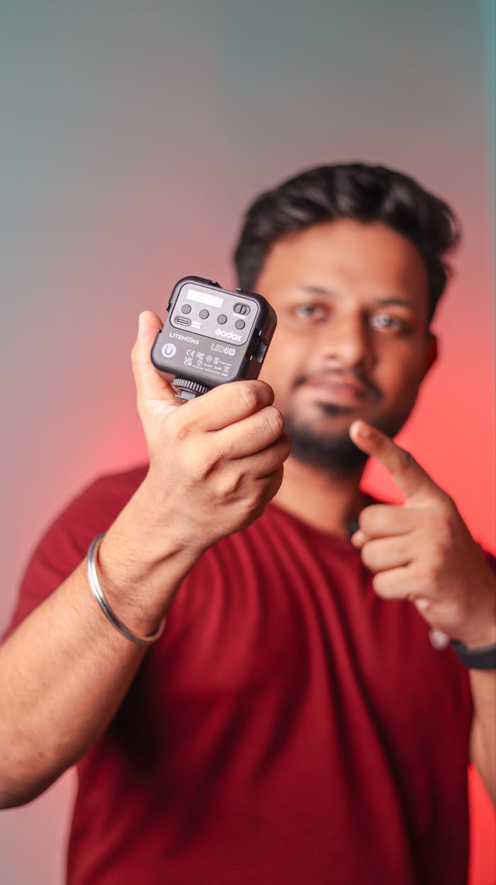 A man in a red shirt showcasing a small electronic gadget with a focused expression.