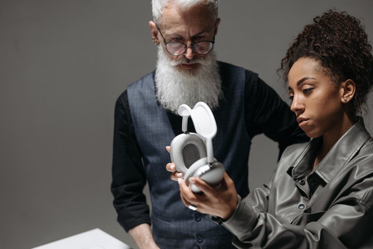 A mature man and a young woman analyze sleek wireless headphones in a corporate setting.
