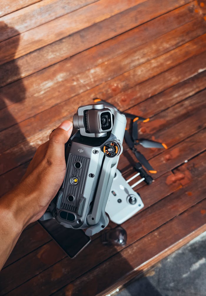 A close-up of a hand holding a drone against a wooden background outdoors.